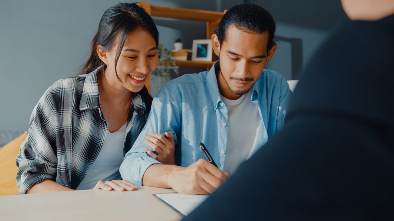 Happy asian young customer couple ready sign bank loan agreement for new house with broker agent, smiling husband and wife consider finance investment insurance contract together in front of broker.